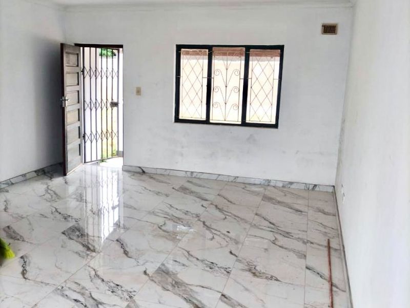 An empty living room featuring polished marble-look floor tiles, a security gate, and a window with security bars.