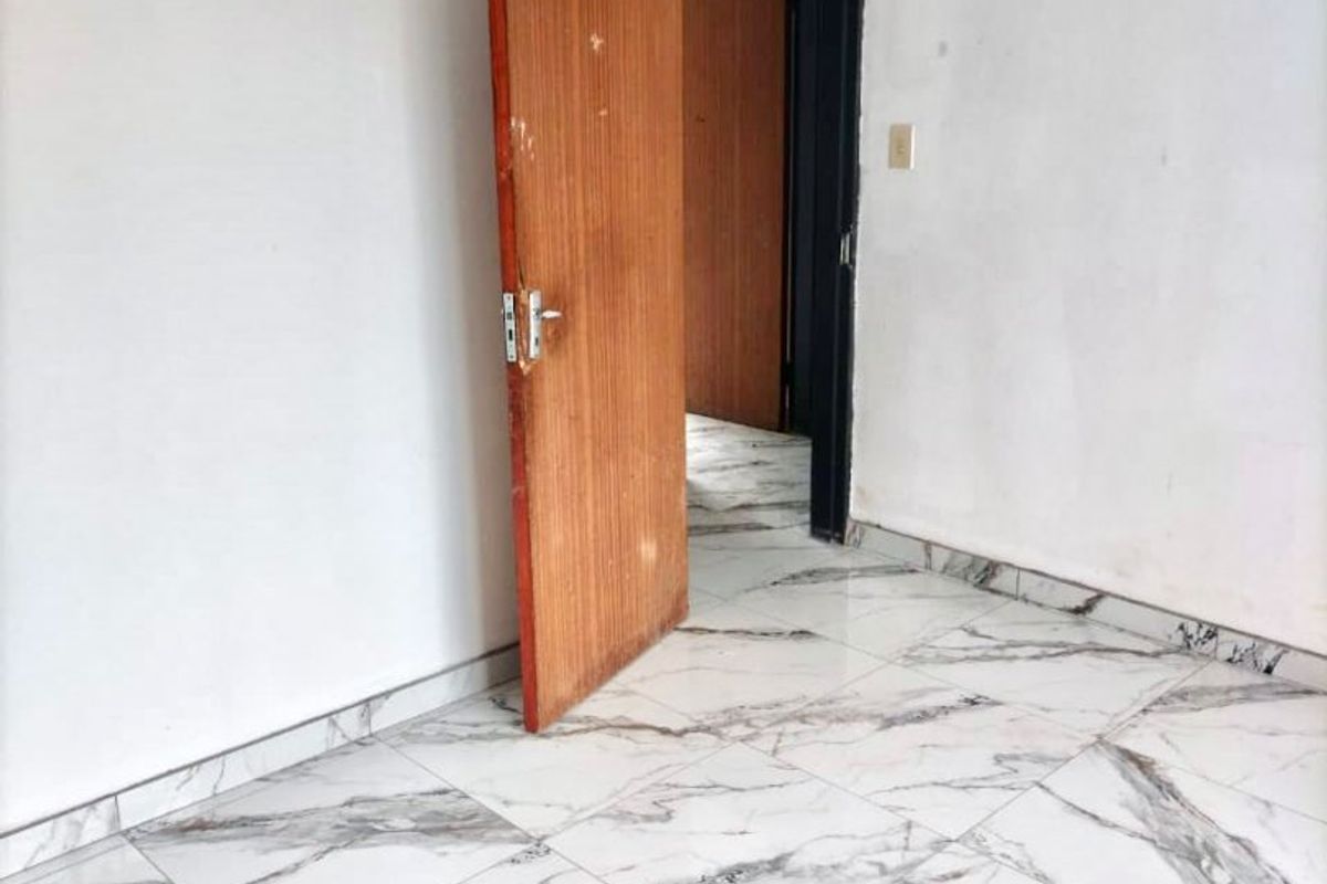 An empty bedroom featuring modern marble-look floor tiles and a wooden door, providing a clean, neutral canvas for interior design.