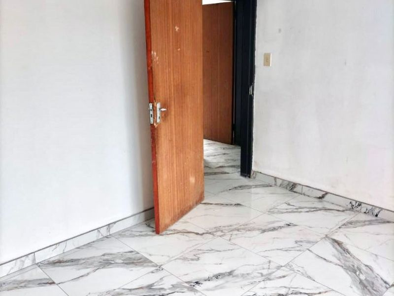 An empty bedroom featuring modern marble-look floor tiles and a wooden door, providing a clean, neutral canvas for interior design.