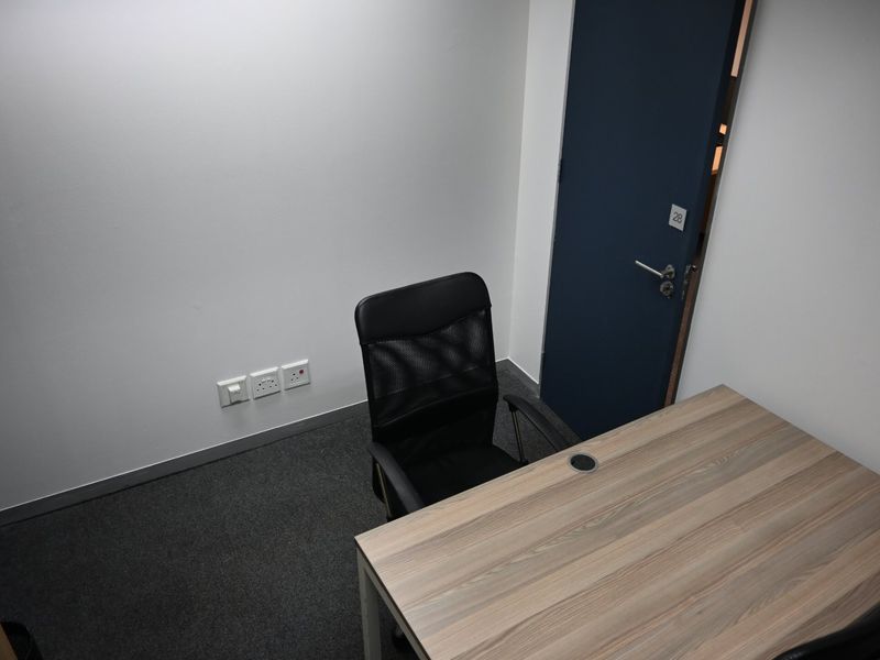 A compact, functional office space featuring neutral walls, carpeted flooring, and a standard internal door.