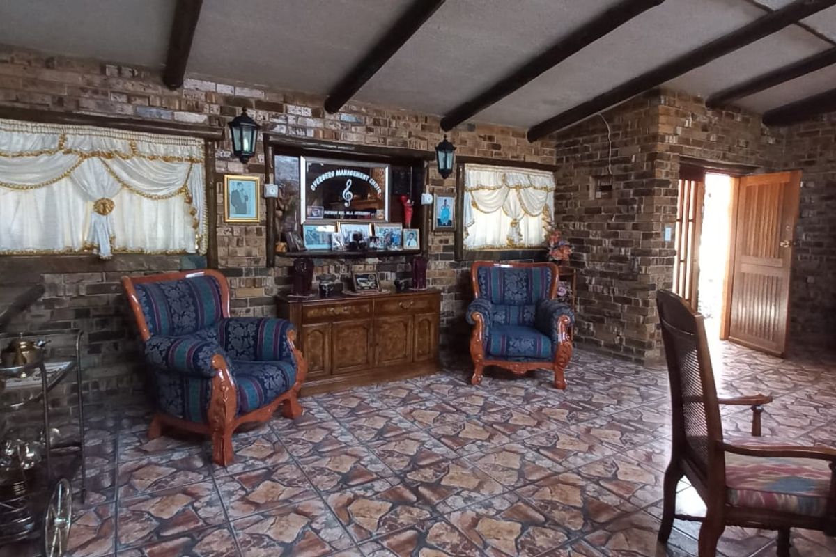 Spacious living area featuring rustic facebrick walls, exposed timber ceiling beams, and durable tiled flooring with direct access to an exterior door.
