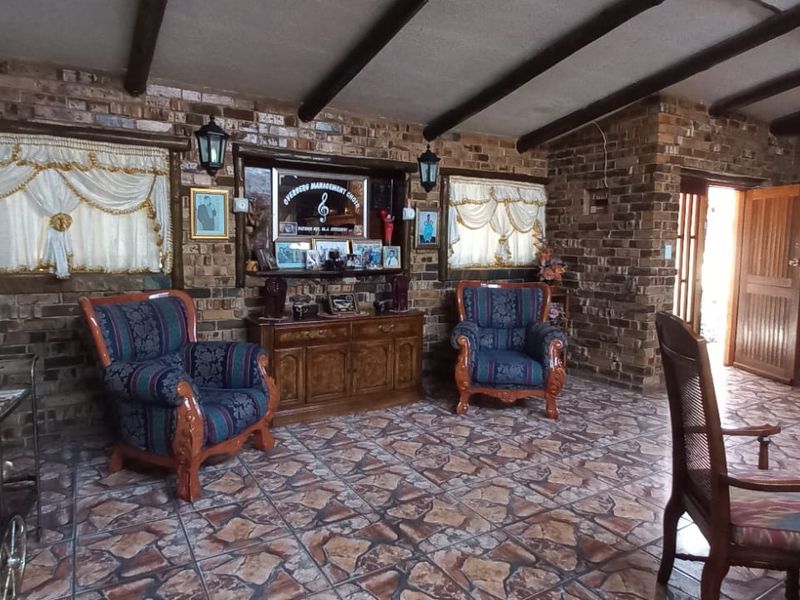 Spacious living area featuring rustic facebrick walls, exposed timber ceiling beams, and durable tiled flooring with direct access to an exterior door.