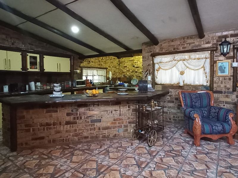 Spacious open-plan living area featuring exposed timber beams, rustic brick walls, and a built-in brick bar counter with tiled flooring throughout.