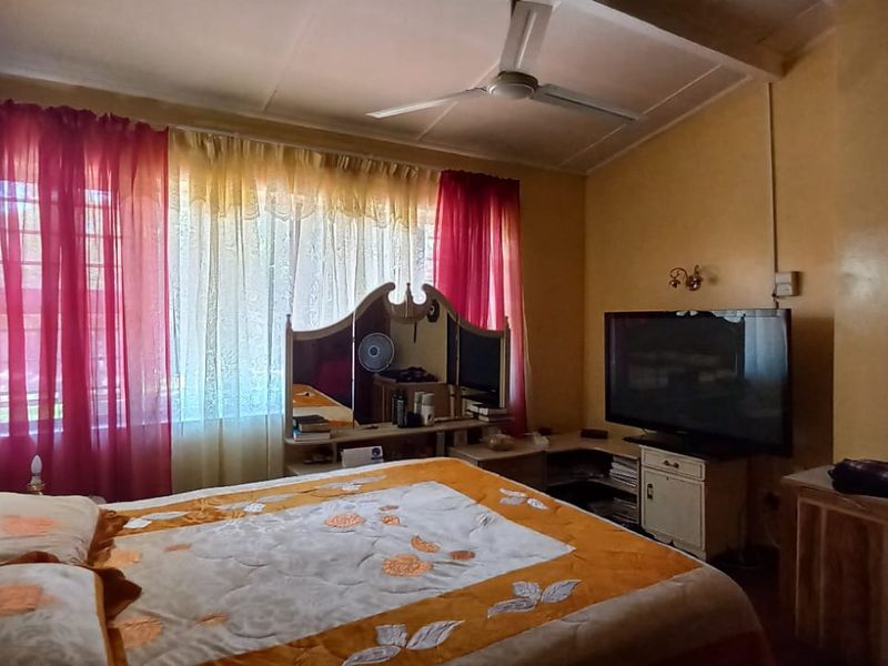 A bedroom featuring a ceiling fan, wall-mounted lighting, and window security bars, offering a functional space with potential for modern updates.