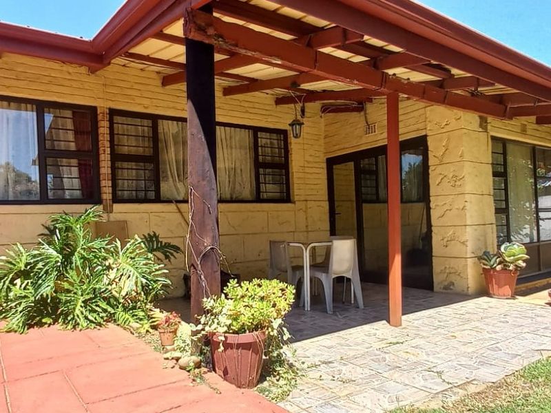 A covered outdoor patio area featuring timber structural elements, stone-tiled flooring, and direct access to the garden through large aluminium-framed windows.