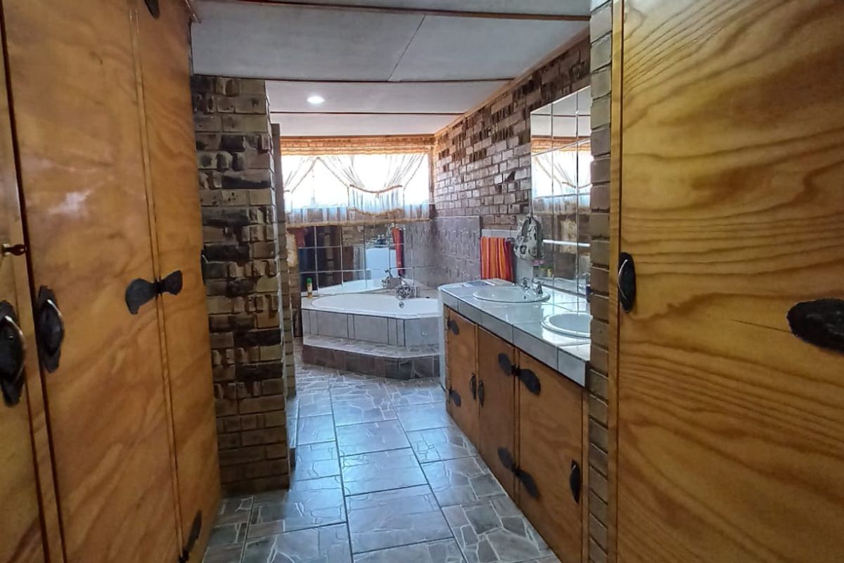 A dated bathroom featuring exposed brick walls, built-in wooden cabinetry with dual vanity basins, and a sunken bathtub.