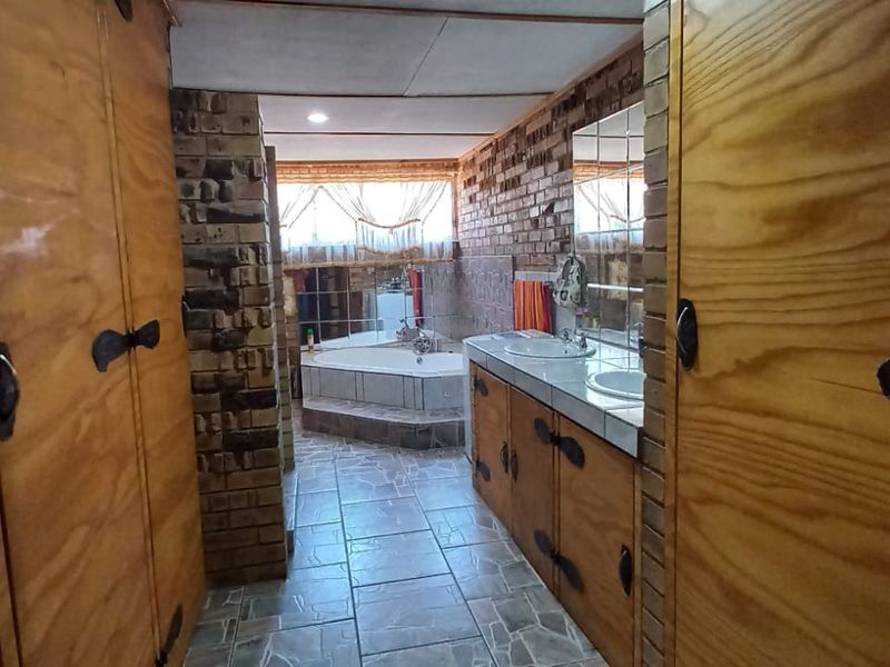 A dated bathroom featuring exposed brick walls, built-in wooden cabinetry with dual vanity basins, and a sunken bathtub.