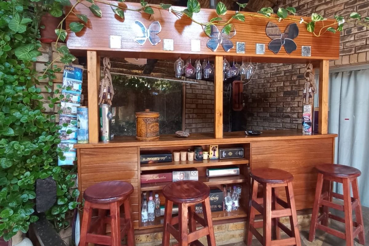 A rustic built-in wooden bar area featuring exposed brick walls and integrated glass storage, situated in a covered patio or entertainment space.