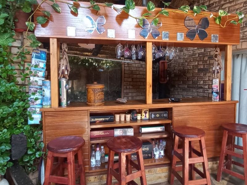 A rustic built-in wooden bar area featuring exposed brick walls and integrated glass storage, situated in a covered patio or entertainment space.