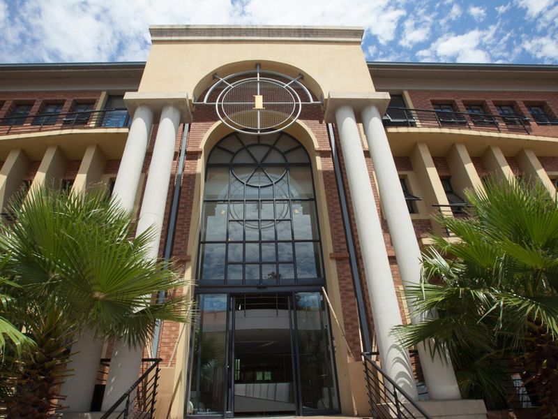 A grand commercial building entrance featuring a brick facade, prominent classical columns, and a large glass entryway with a decorative metal architectural element.