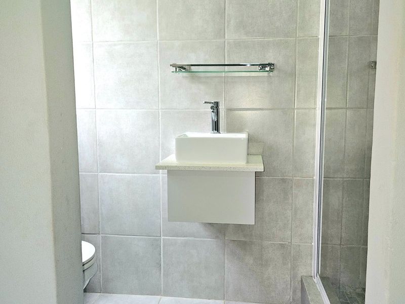 A clean, modern bathroom featuring a wall-mounted vanity with a vessel sink, tiled surfaces, and a glass-enclosed shower.