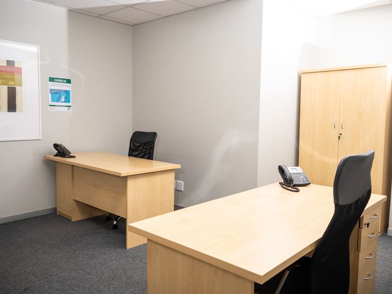 A functional commercial office space featuring neutral wall finishes, carpeted flooring, and a suspended ceiling, suitable for professional use.