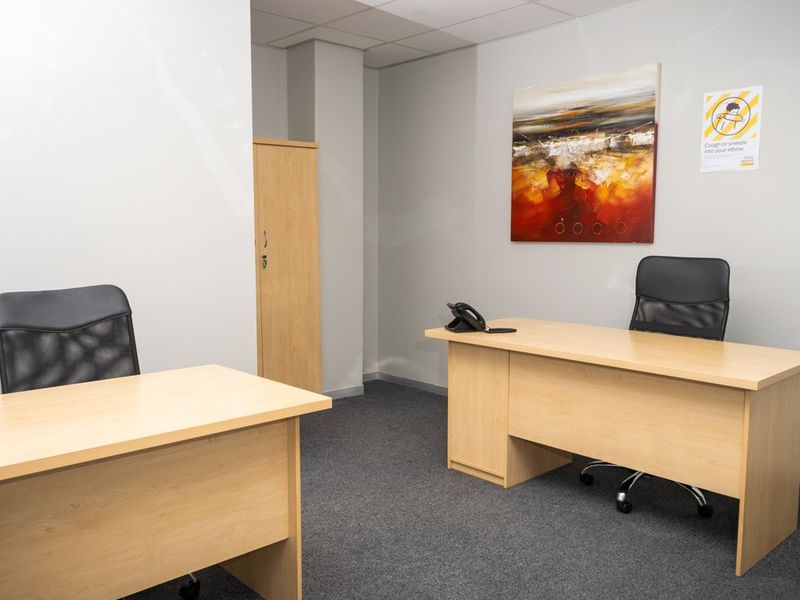 A functional commercial office space featuring neutral wall finishes, carpeted flooring, and a built-in storage cupboard.