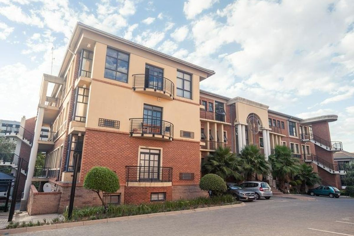 A multi-story commercial building featuring a brick and stucco facade, external staircases, private balconies with metal railings, and an adjacent paved parking area.