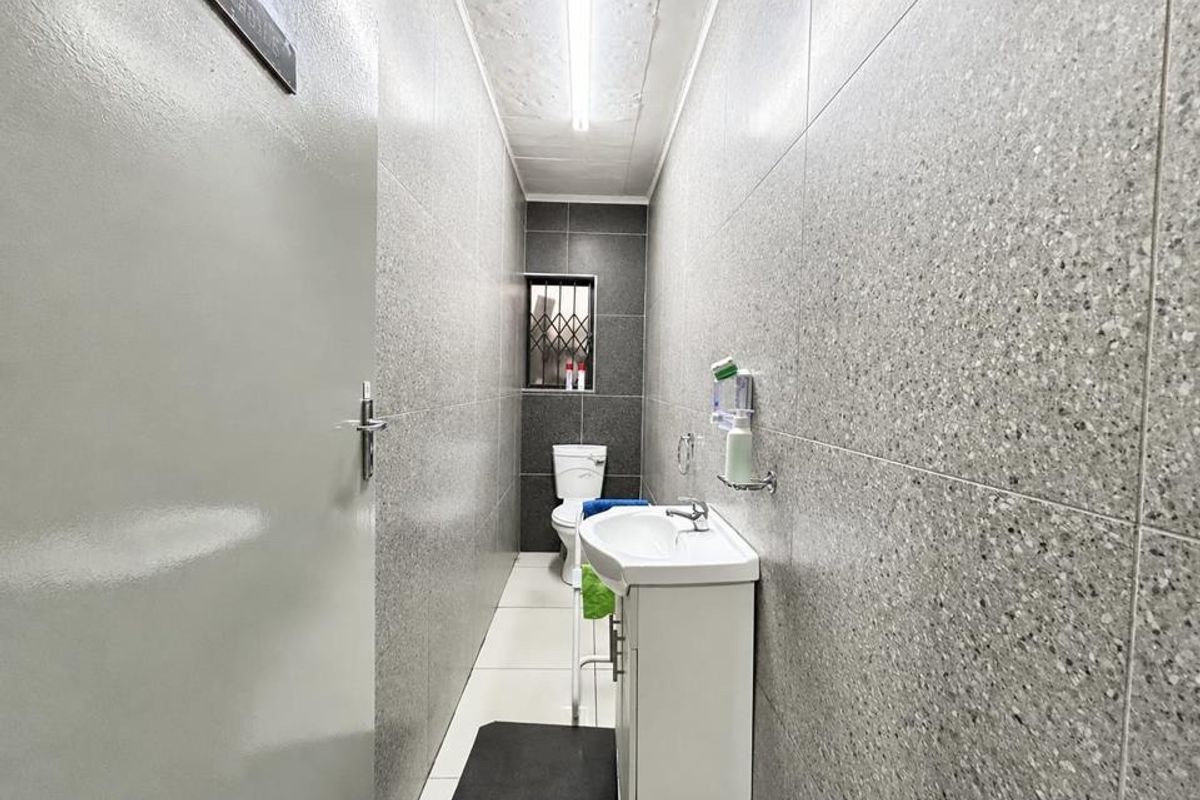 A compact, functional bathroom featuring full-height grey speckled wall tiling, a white vanity basin, and a standard toilet.