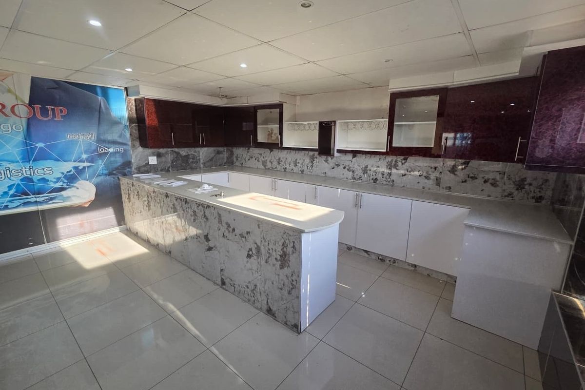 A modern, clean kitchen area featuring extensive built-in cabinetry, stone-look countertops, and a drop ceiling with recessed lighting in an industrial office setting.