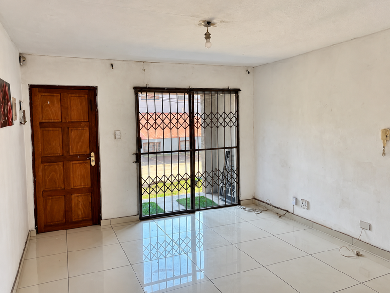 An empty living room featuring tiled flooring, a wooden entrance door, and a security gate leading to an outdoor area.