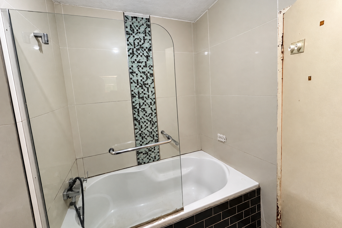 Bathroom featuring a bathtub with a glass shower screen, mosaic tile accent, and black subway tile surround. Requires minor cosmetic repairs to the door frame.