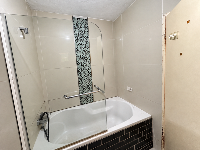 Bathroom featuring a bathtub with a glass shower screen, mosaic tile accent, and black subway tile surround. Requires minor cosmetic repairs to the door frame.
