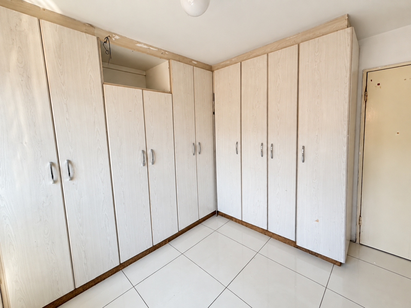 Bedroom featuring extensive built-in cabinetry with light wood-grain finish and tiled flooring, currently requiring minor repairs to cupboard doors and trim.