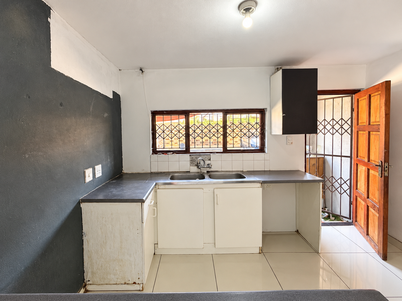 A functional kitchen area featuring a double basin sink, tiled splashback, and built-in cabinetry, with direct access to an exterior security gate.
