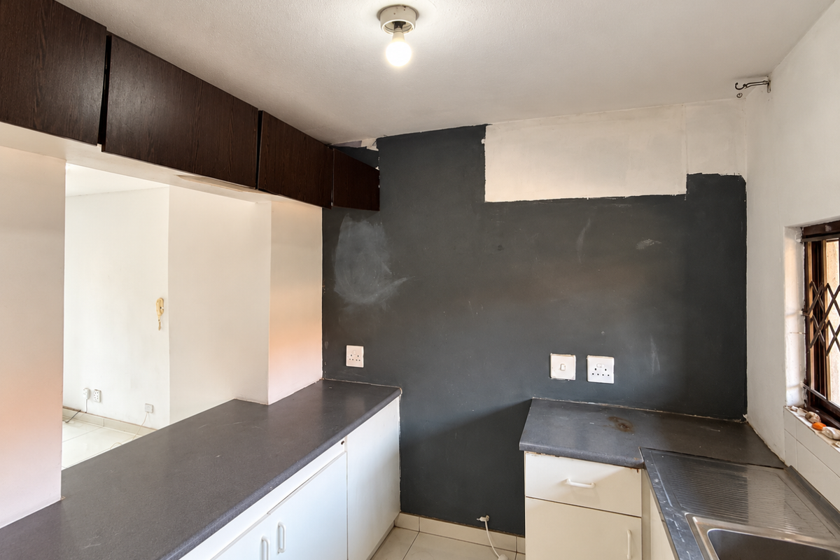 A compact kitchen featuring built-in cabinetry, dark countertops, and a stainless steel sink, currently requiring cosmetic updates and wall finishing.