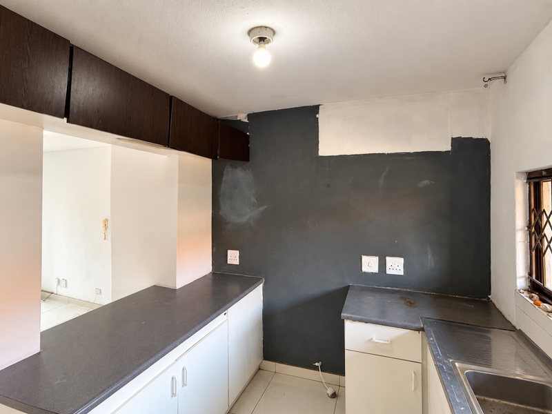 A compact kitchen featuring built-in cabinetry, dark countertops, and a stainless steel sink, currently requiring cosmetic updates and wall finishing.