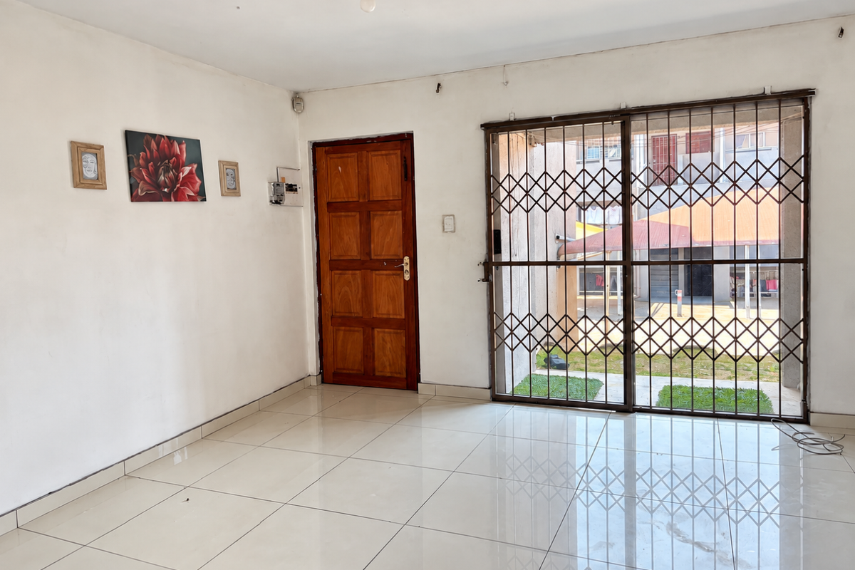 An open-plan living area featuring polished tile flooring, a secure metal gate, and a solid wooden entrance door, offering a clean and functional space.