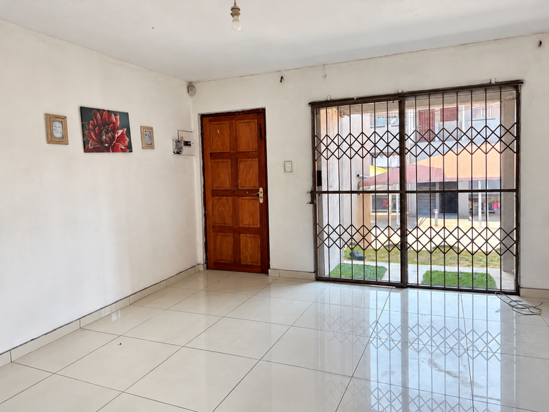 An open-plan living area featuring polished tile flooring, a secure metal gate, and a solid wooden entrance door, offering a clean and functional space.