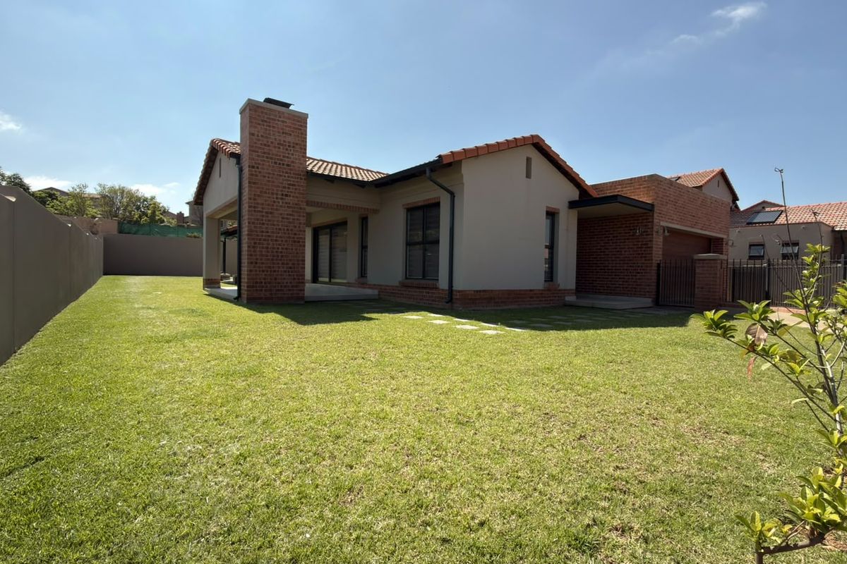 Rear view of a modern house featuring a brick chimney, covered patio, and a well-maintained lawn enclosed by a boundary wall.