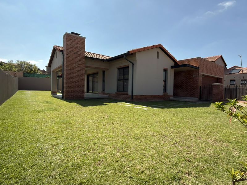 Rear view of a modern house featuring a brick chimney, covered patio, and a well-maintained lawn enclosed by a boundary wall.