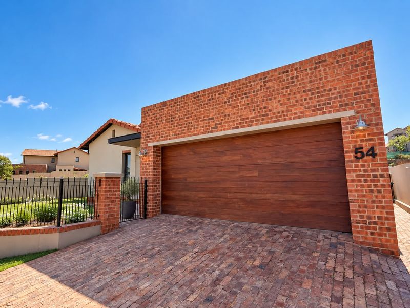 Front elevation featuring a modern brick facade, a large wooden-finish sectional garage door, and a neatly paved driveway with secure perimeter fencing.
