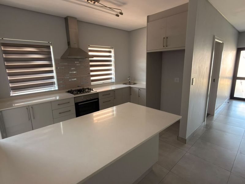 Modern kitchen featuring stone countertops, a central island, built-in gas hob, oven, extractor fan, and tiled flooring in a clean, open-plan layout.