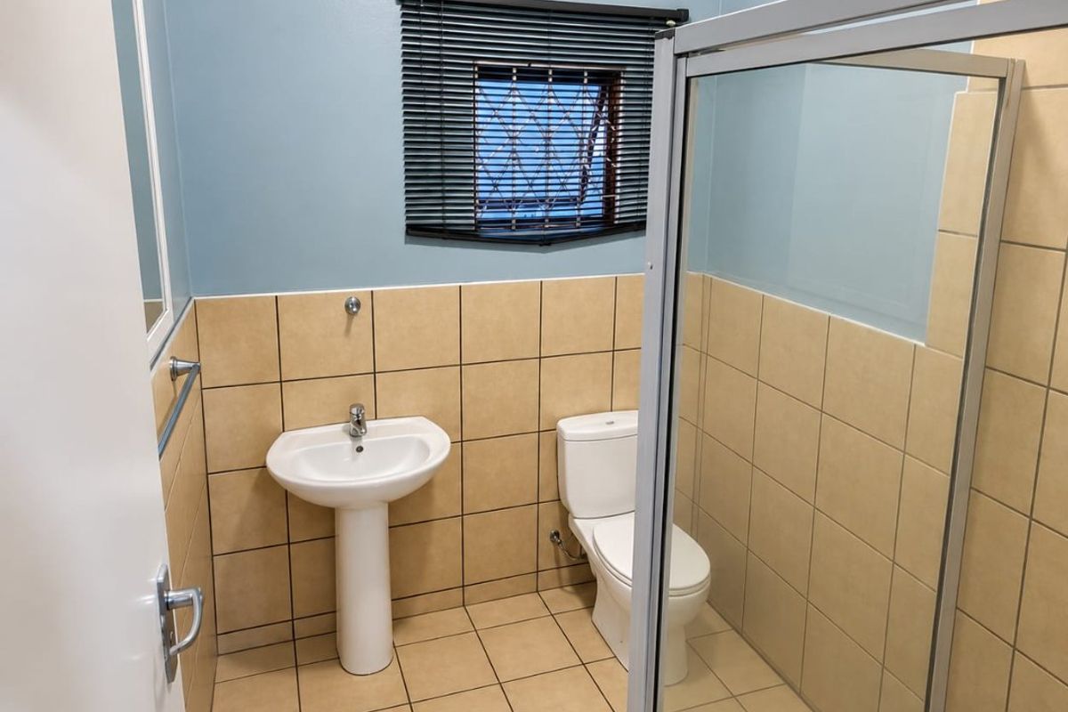 A clean and functional bathroom featuring a pedestal basin, toilet, and a glass-enclosed shower with neutral ceramic tiling.