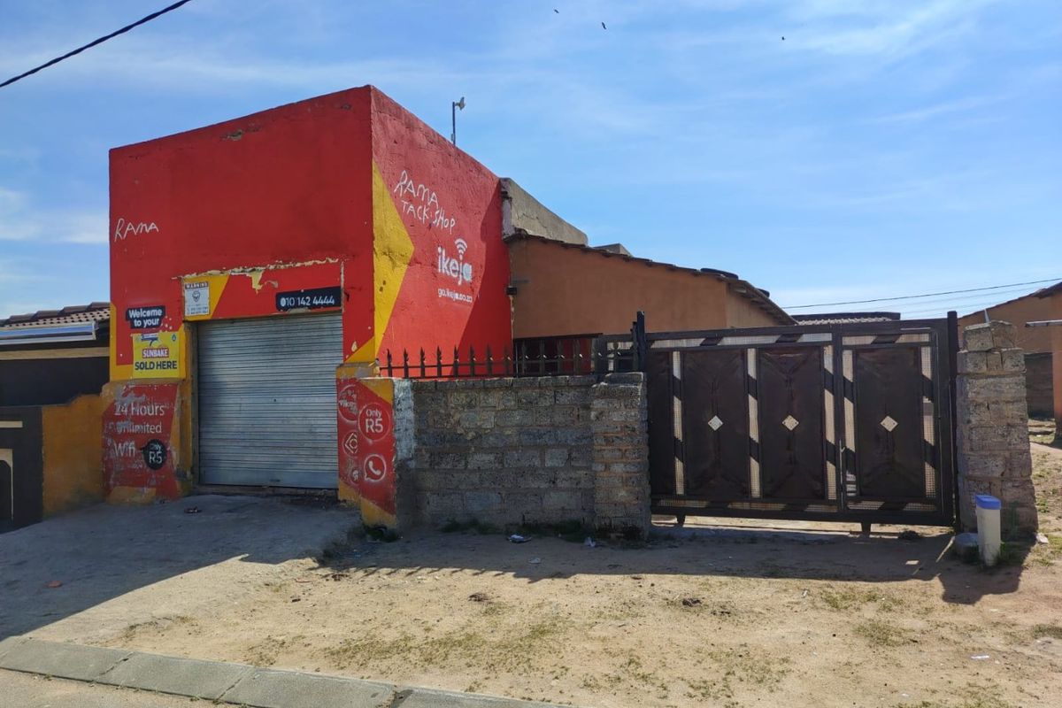 Front elevation of a property featuring a roller shutter door, metal security gate, and masonry boundary wall with visible exterior wear.