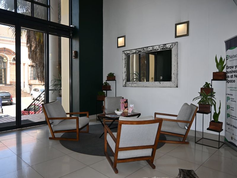 A bright and modern commercial entrance area featuring large glass sliding doors, tiled flooring, and contemporary wall lighting.