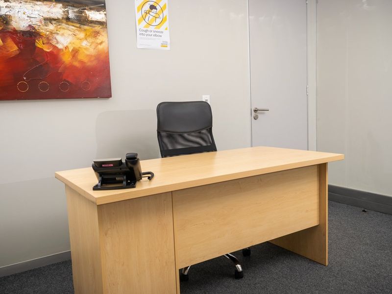 A functional commercial office space featuring neutral wall finishes, carpet flooring, and a standard internal door.