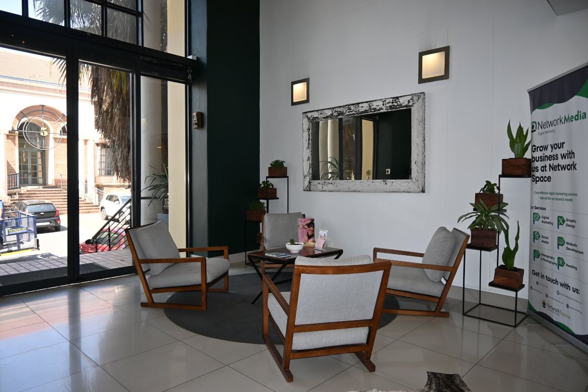 A bright and modern commercial entrance area featuring large glass sliding doors, tiled flooring, and contemporary wall lighting.