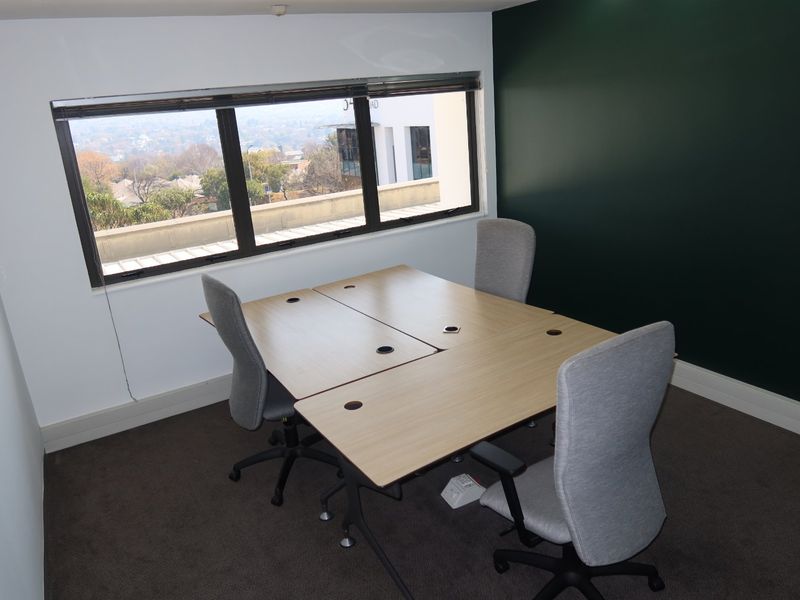 A functional office space featuring a large window with exterior views, dark carpeting, and a dark green accent wall.
