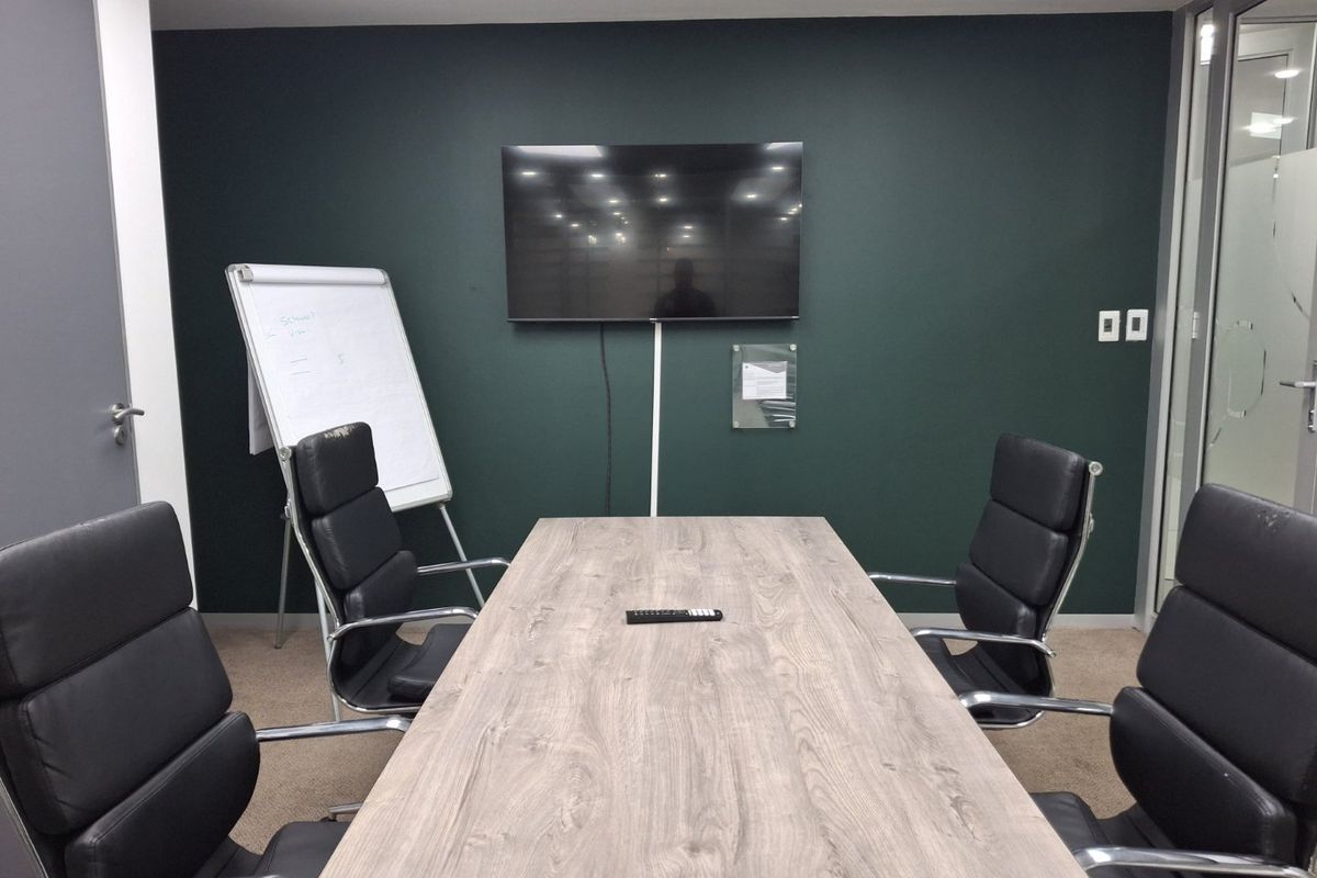 A professional meeting room featuring a dark accent wall, suspended ceiling, and glass partition, suitable for collaborative business use.