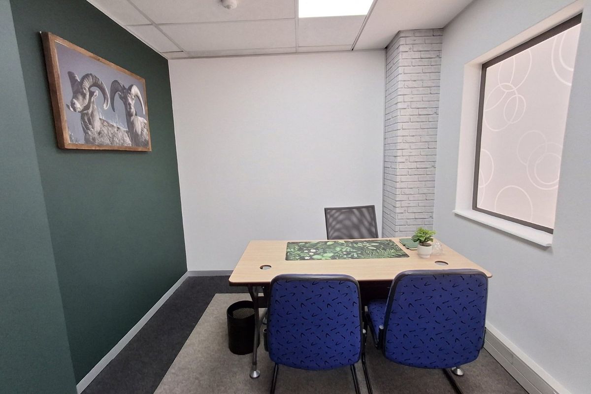 A compact, well-maintained office space featuring a modern dark green accent wall, exposed brick detailing, and a suspended ceiling with recessed lighting.