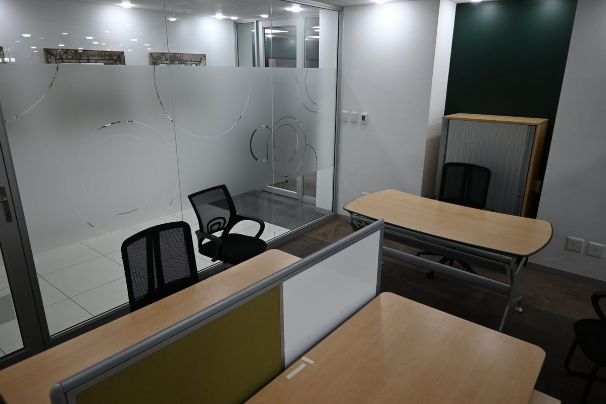 A modern commercial office space featuring a glass partition wall with decorative frosted film, recessed lighting, and functional workspace layout.