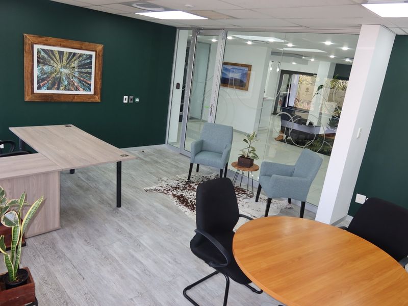 Modern commercial office space featuring a glass partition wall, recessed ceiling lighting, and durable laminate flooring, creating a professional and open work environment.
