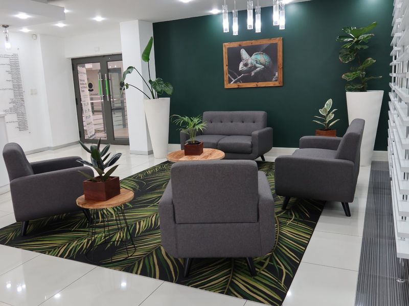 A modern commercial reception or waiting area featuring polished tiled floors, a dark green accent wall, and contemporary recessed lighting.