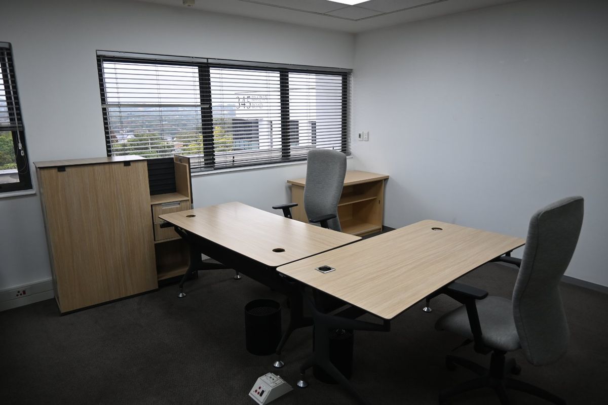 A functional commercial office space featuring neutral carpet flooring, recessed ceiling lighting, and large windows with venetian blinds providing natural light.