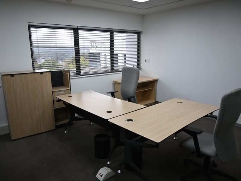A functional commercial office space featuring neutral carpet flooring, recessed ceiling lighting, and large windows with venetian blinds providing natural light.