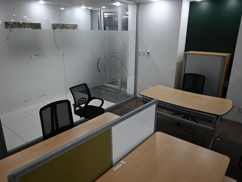 A modern commercial office space featuring a glass partition wall with decorative frosted film, recessed lighting, and functional workspace layout.