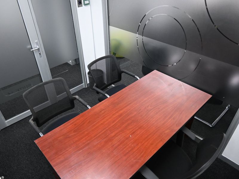 A compact, modern office meeting room featuring a frosted glass partition, aluminium door frame, and dark carpet flooring.