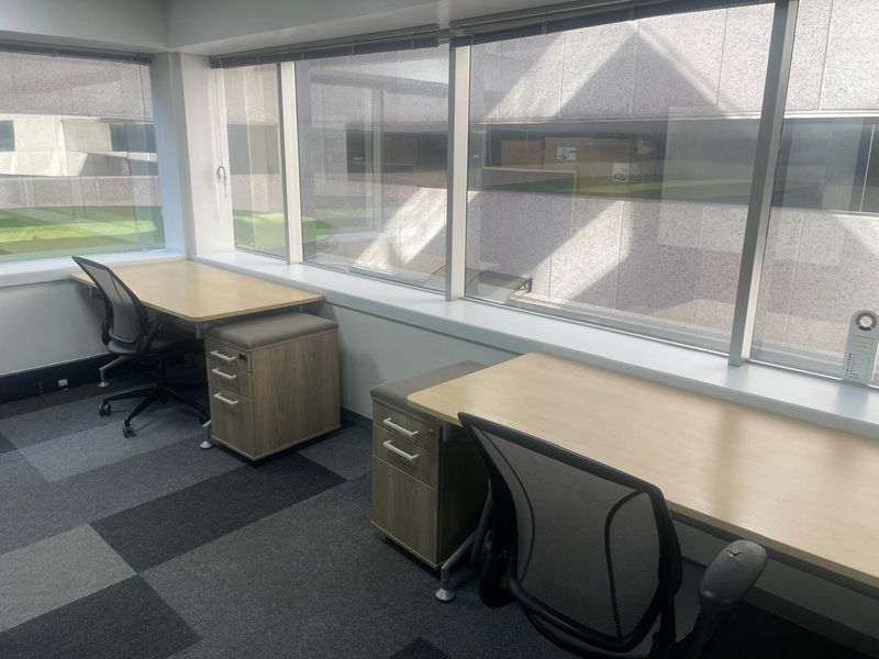 A bright commercial office space featuring large windows with blinds and modern carpet tiles, providing a functional workspace environment.