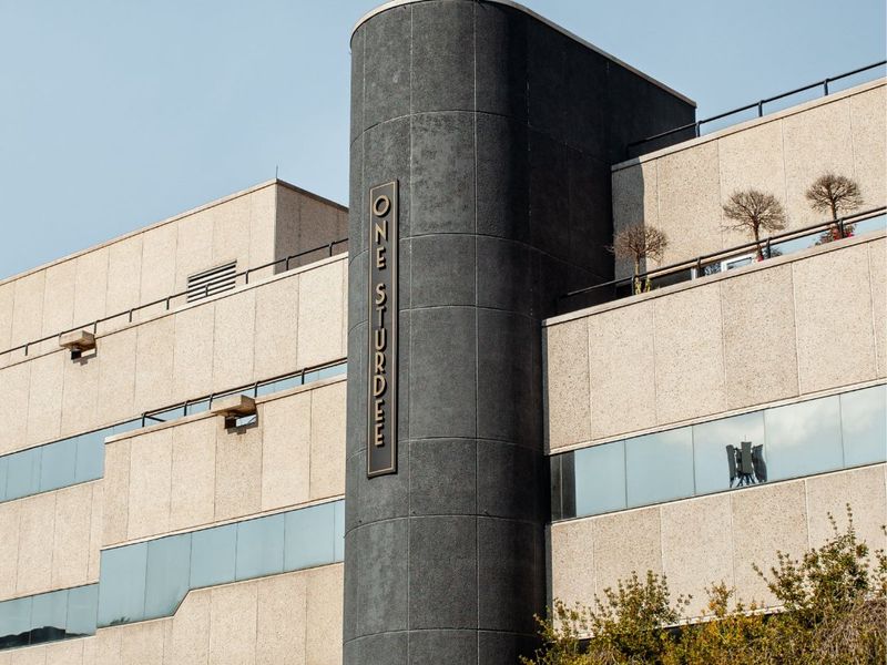 Exterior view of the One Sturdee commercial building featuring a modern concrete facade, ribbon windows, and a rooftop terrace area.